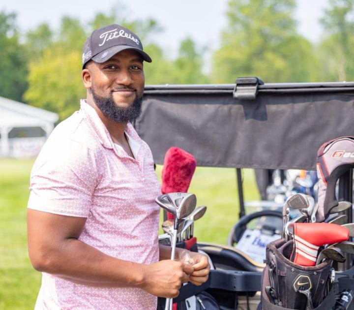 Man standing with golf clubs by a golf cart